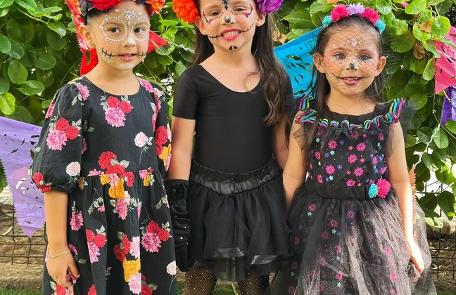 Tres alumnas de kínder maquilladas de catrina frente al altar de Día de Muertos