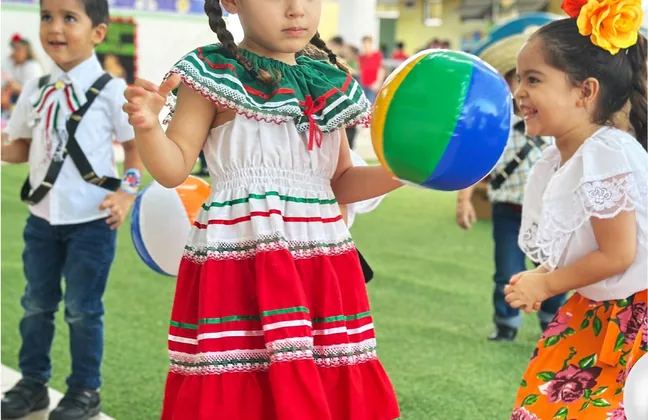 Alumnos de kínder con trajes típicos mexicanos jugando con una pelota en el patio