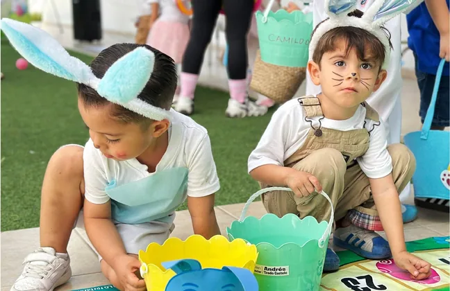 Alumnos de kínder con orejas de conejo buscando huevos de Pascua en el jardín