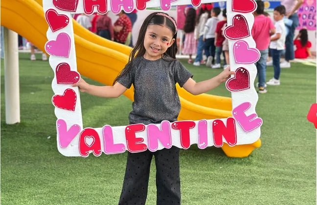 Alumna de kínder posando en un marco decorado por el Día del Amor y la Amistad
