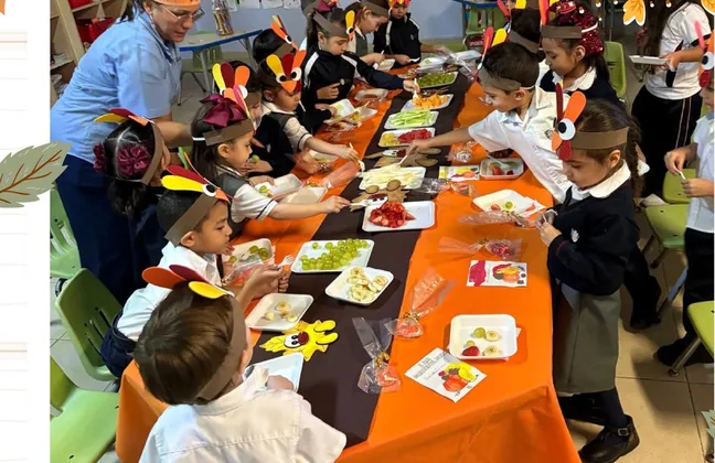 Alumnos de kínder compartiendo la comida de Thanksgiving en una mesa larga